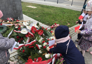Dziewczynka kładzie flagę Polski pod pomnikiem.