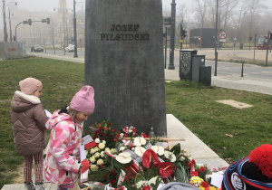 Dziewczynki kładą flagę Polski pod pomnikiem.
