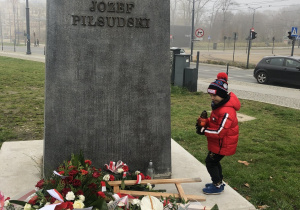 Chłopiec kładzie znicz pod pomnikiem Marszałka Józefa Piłsudkiego.