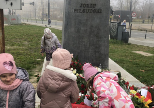Dzieci kładą flagę Polski pod pomnikiem.