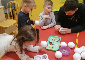 Rodzice z dziećmi mocują elementy dekoracyjne na styropianowej bombce.