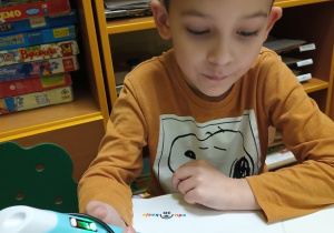 Chłopiec rysuje bombkę długopisem do druku 3D przy stoliku.