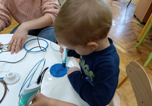 Chłopiec rysuje bombkę długopisem do druku 3D przy stoliku.