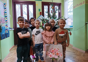 Dzieci stoją przy choince z prezentami od Mikołaja.