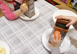 Dziewczynka ściera na tarce marchewkę.
