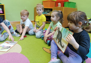 Dzieci siedzą i oglądają obrazek z kotem.