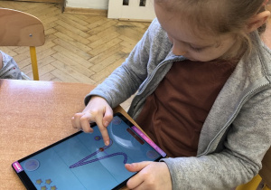 Dziewczynka pisze litery na aplikacji na tablecie.